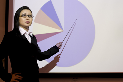 A picture of a woman giving a presentation that contains a pie chart.